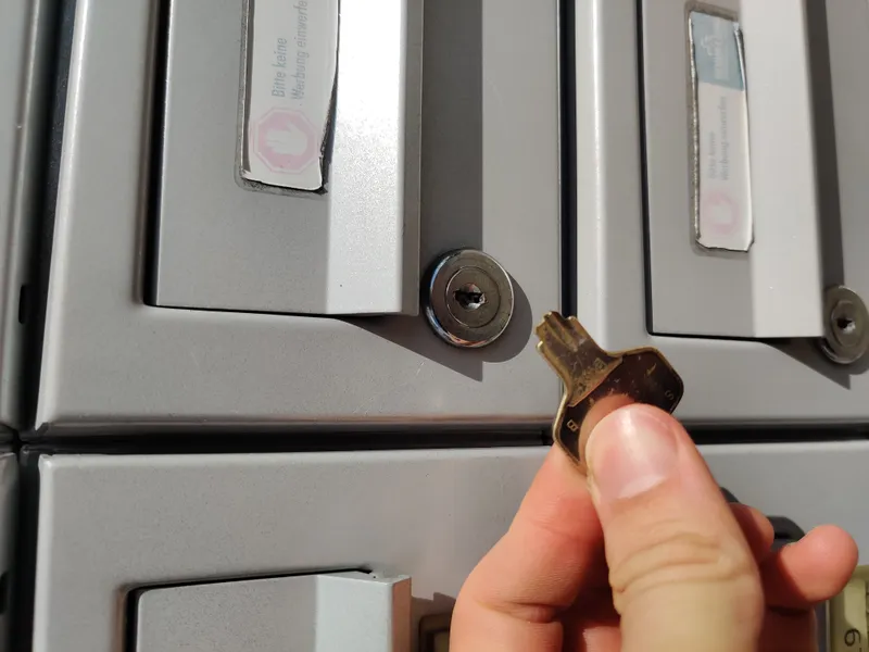 Hand hält einen Schlüssel vor dem Schloss einer grauen Briefkastenanlage