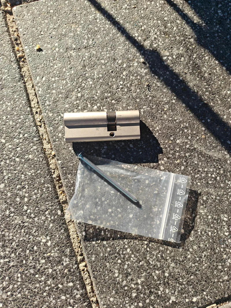 Ausgebauter Profilzylinder mit Werkzeug im Beutel auf Asphalt nach dem Zylinderwechsel