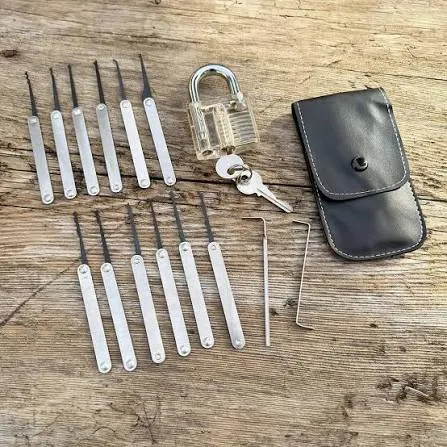 Dietrich-Set mit Picks und Spannwerkzeug neben einem durchsichtigen Vorhängeschloss auf Holz