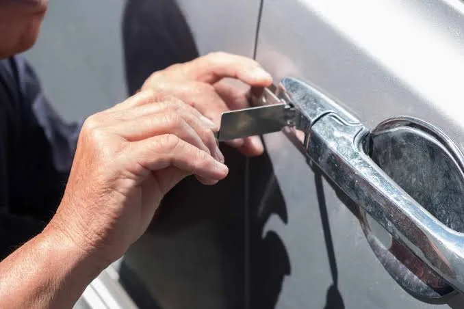Hände öffnen eine verschlossene Autotür am verchromten Türgriff mit einem Flachwerkzeug